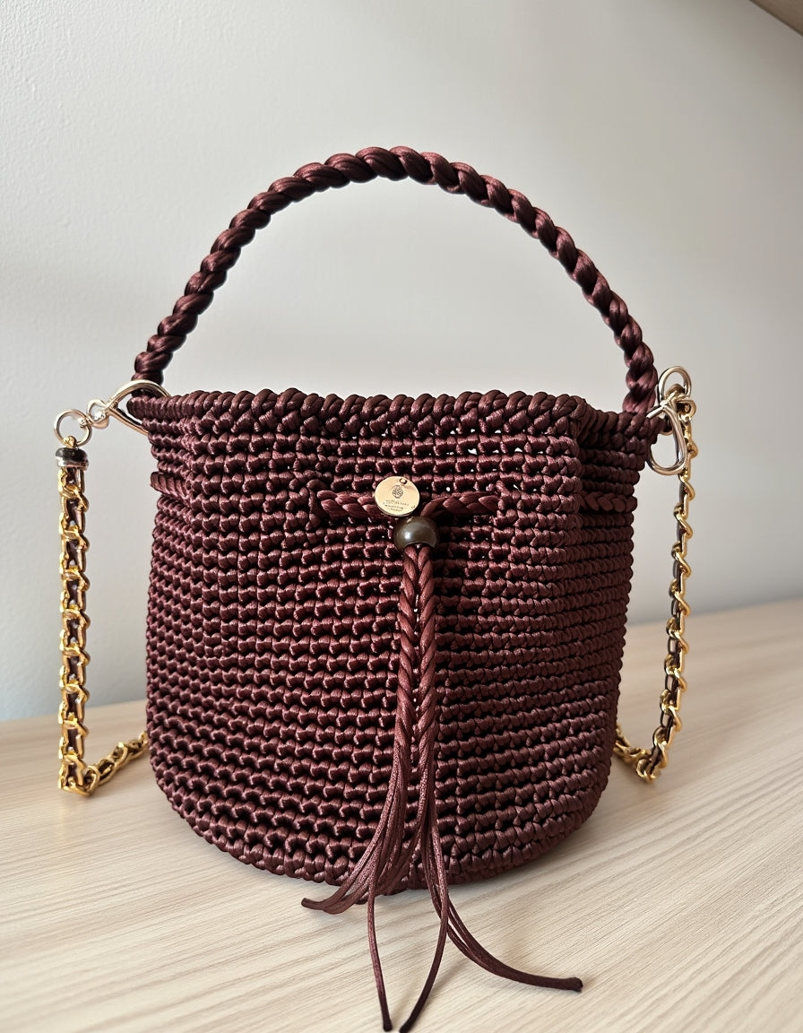 Bolso artesanal color vino con cordón frontal y cadena metálica dorada.