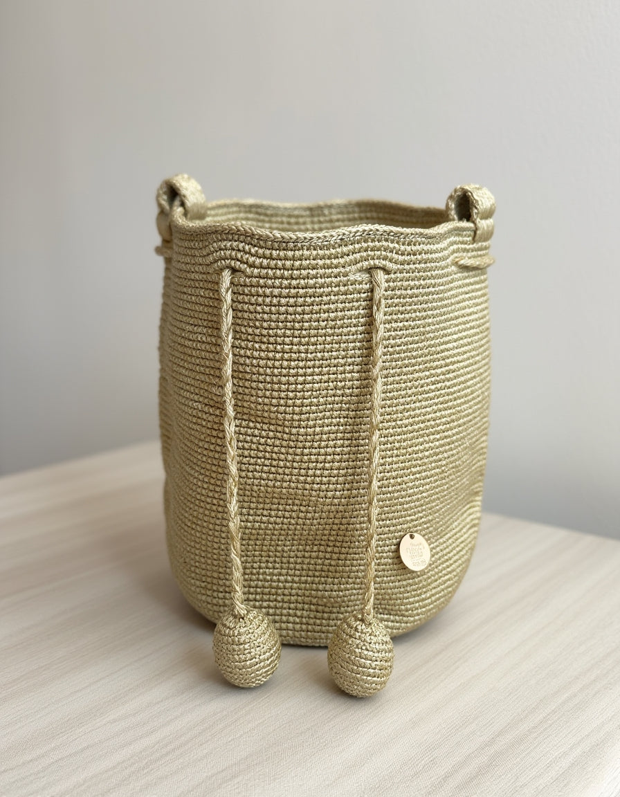 Bolso natural tejido a mano, en color dorado tierra, con pompones largos y estilo elegante.