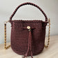 Bolso artesanal color vino con cordón frontal y cadena metálica dorada.