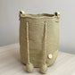 Bolso natural tejido a mano, en color dorado tierra, con pompones largos y estilo elegante.