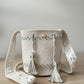Bolso mochila tejido a mano en blanco perla con detalles bordados en azul y gris.