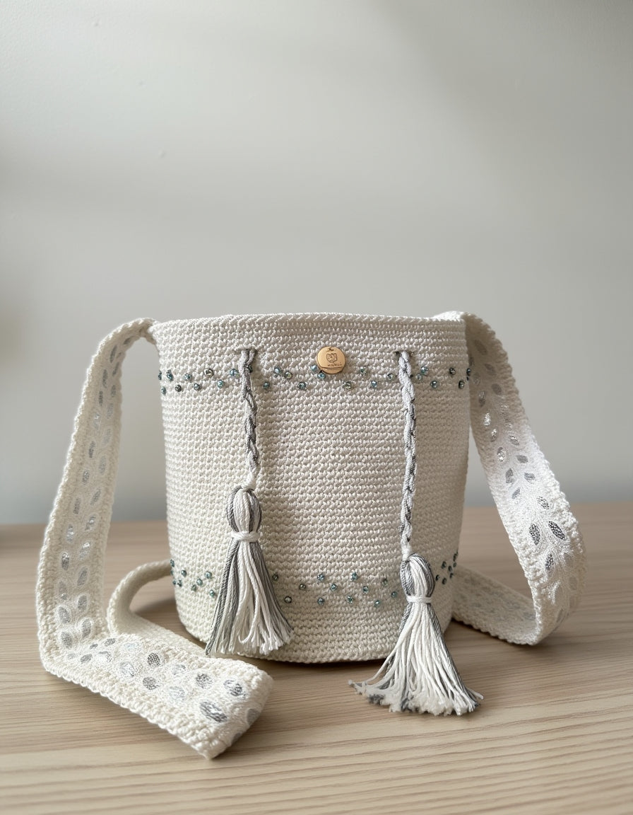 Bolso mochila tejido a mano en blanco perla con detalles bordados en azul y gris.