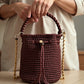 Mochila de lujo tono merlot con diseño cilíndrico y textura tejida.