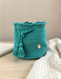 Mochila hecha a mano Domenechsa en color turquesa esmeralda con cierre de cordón y borlas tejidas.
