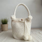 Mochila blanca con perlas y pompones decorativos, ideal para outfits elegantes y modernos.