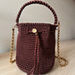Mochila Merlot Elegante tejida a mano con cadena dorada y asa trenzada.