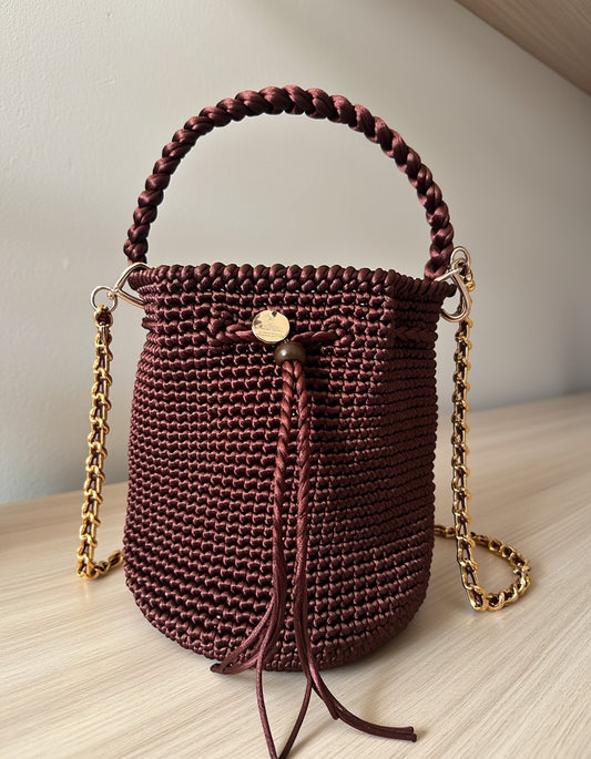 Mochila Merlot Elegante tejida a mano con cadena dorada y asa trenzada.