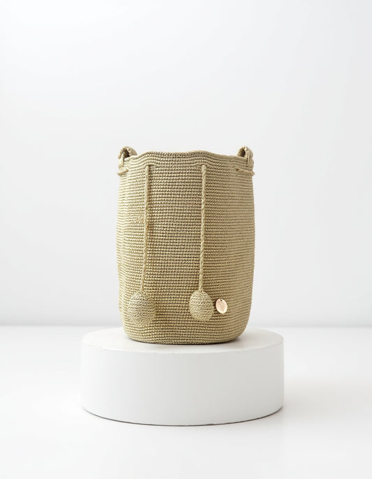 Mochila artesanal Domenechsa en tono oro tierra, tejida a mano con pompones decorativos.