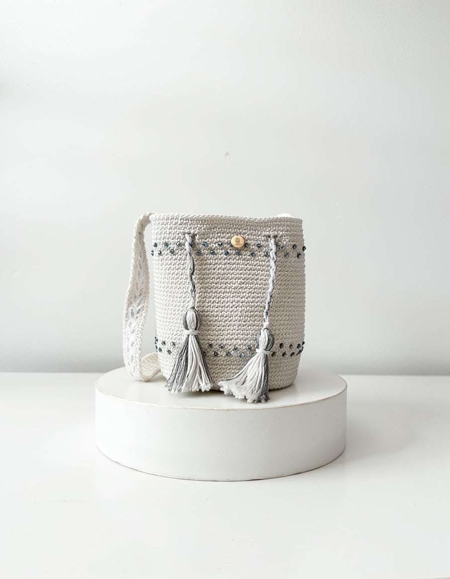 Mochila artesanal en tonos perla y gris con borlas decorativas, diseño Perla Boreal de Domenechsa.