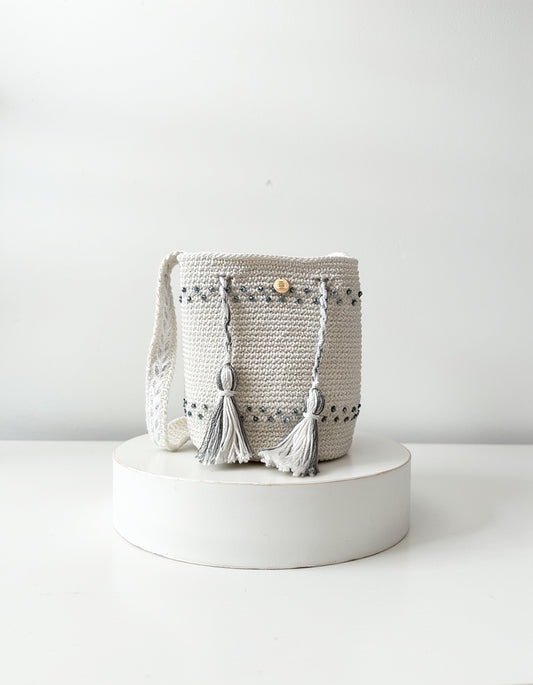 Mochila artesanal en tonos perla y gris con borlas decorativas, diseño Perla Boreal de Domenechsa.